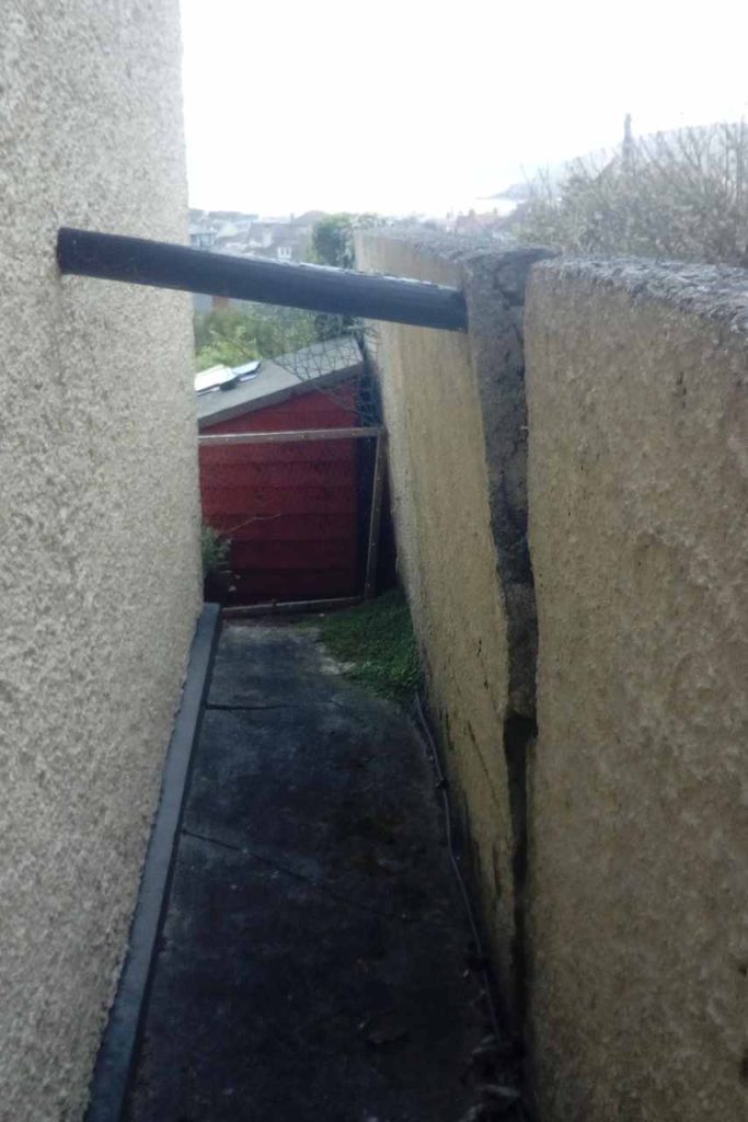 Old failed retaining wall propped up by pipe in between properties